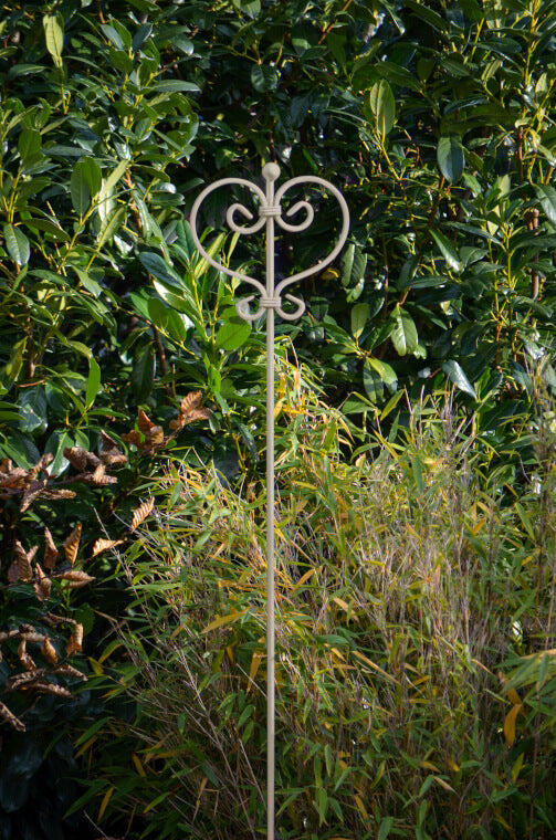 Rankstab Tisssano in pulverbeschichtet Sonderfarbe RAL 9001 Cremeweiß aus der Nähe in einem grün bepflanzten Garten Rankstab Tisssano in pulverbeschichtet Sonderfarbe RAL 9001 Cremeweiß aus der Nähe in einem grün bepflanzten Garten